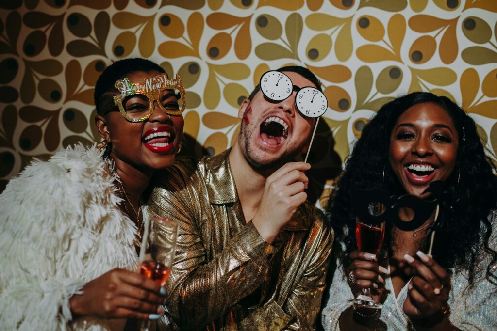 Three friends in festive outfits celebrate New Year's Eve with props and laughter.